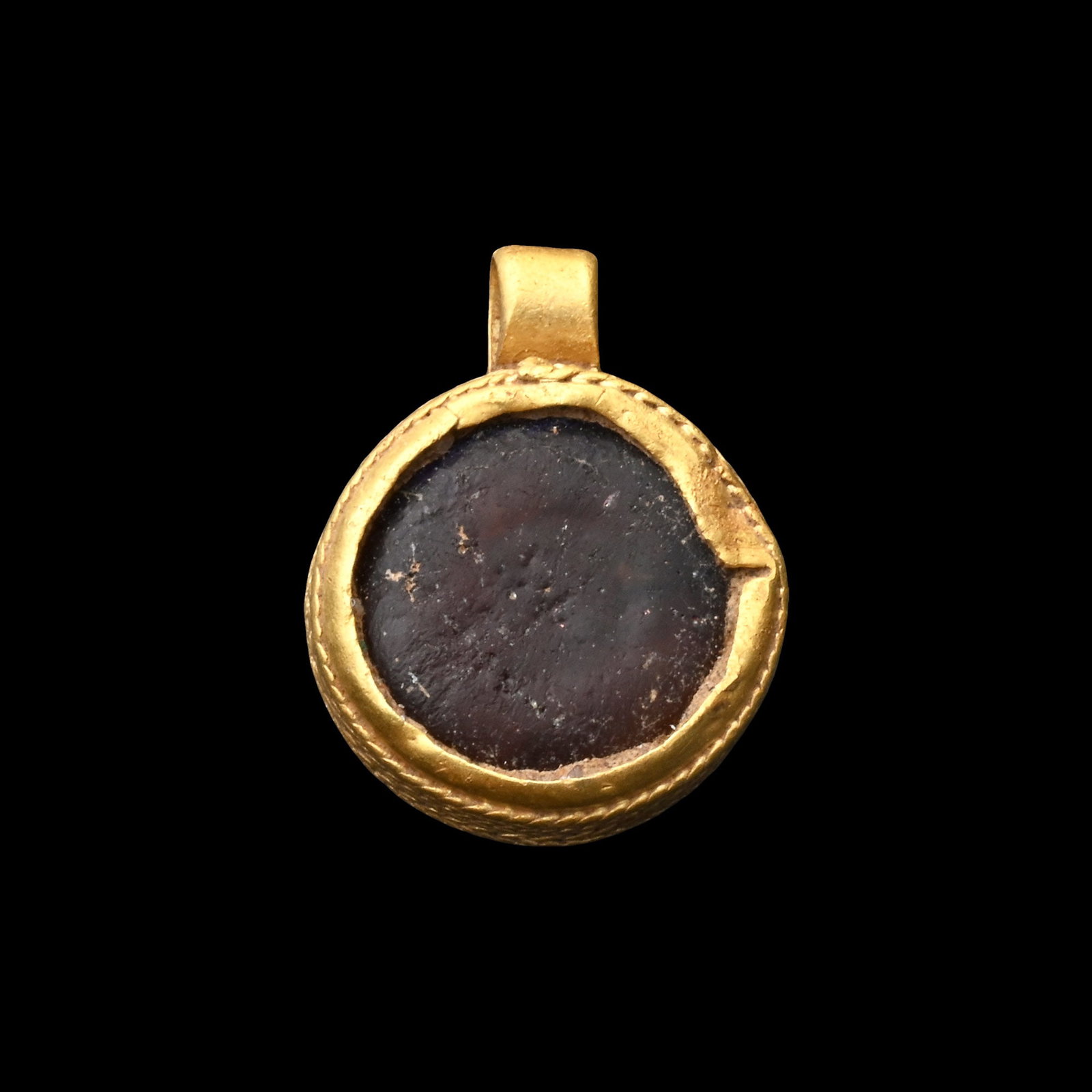 Anglo-Saxon Gold Necklace Pendant with Amber Cabochon: Circa 600-700 A.D. Circular in plan and comprising a thin sheet backing plate with applied tall sides set perpendicular to create a mount for the stone; the sides formed from six bands of twisted wire