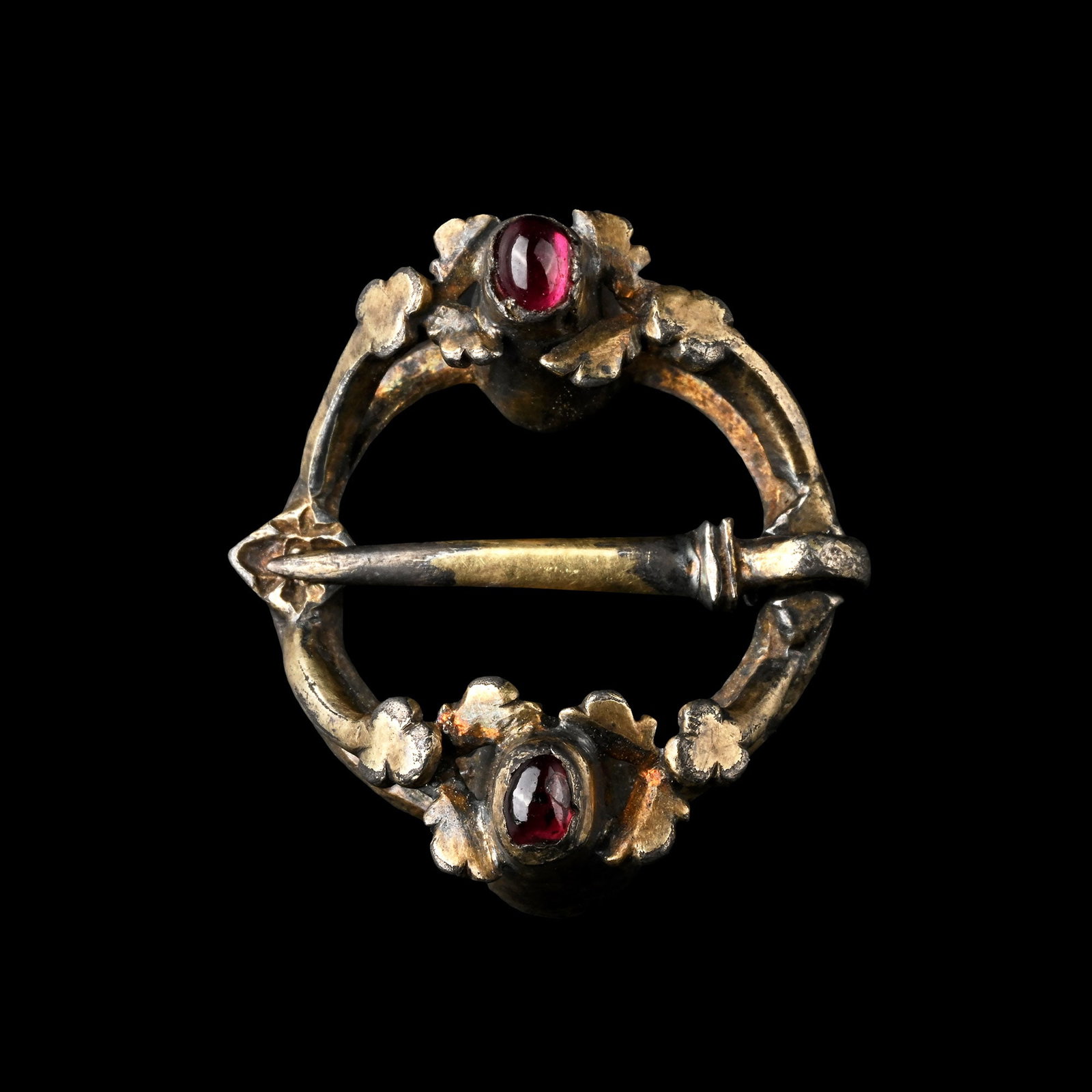 Medieval Silver-Gilt Ring Brooch with Garnet Cabochons: Europe, 13th-14th century A.D. Annular in form with tapering cells to each end, with inset garnet cabochons, and leaf detailing, quatrefoil opposite the sword-shaped pin. Cf. Egan, G. & Pritchard, F.,