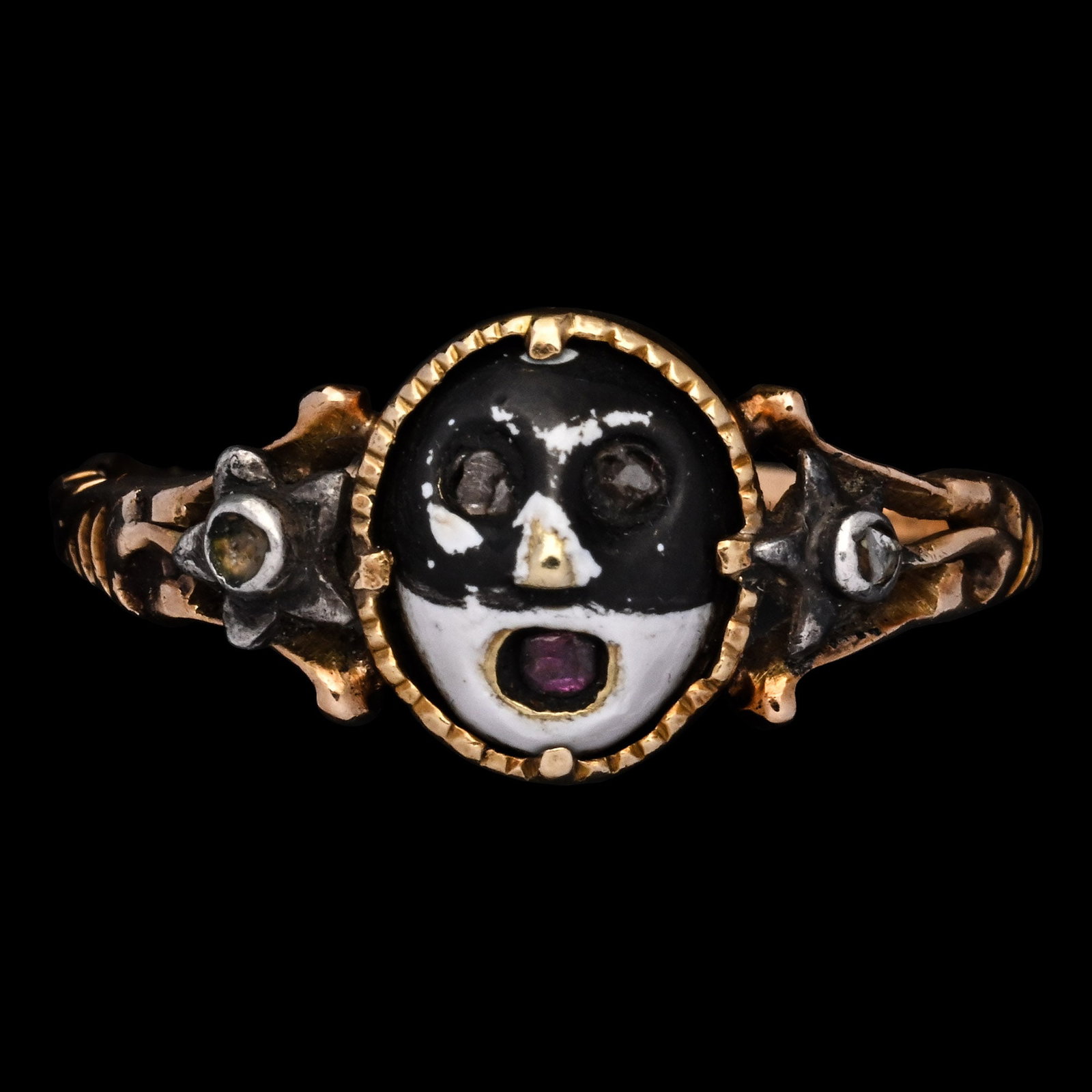 Gem-Set Gold Masquerade Ring with Love Inscription: Italy, circa 1760 A.D. Finely modelled with a black-and-white enamelled mask, the features animated by rose-cut diamond eyes and a small ruby set into the open mouth; the head framed by a serrated gol