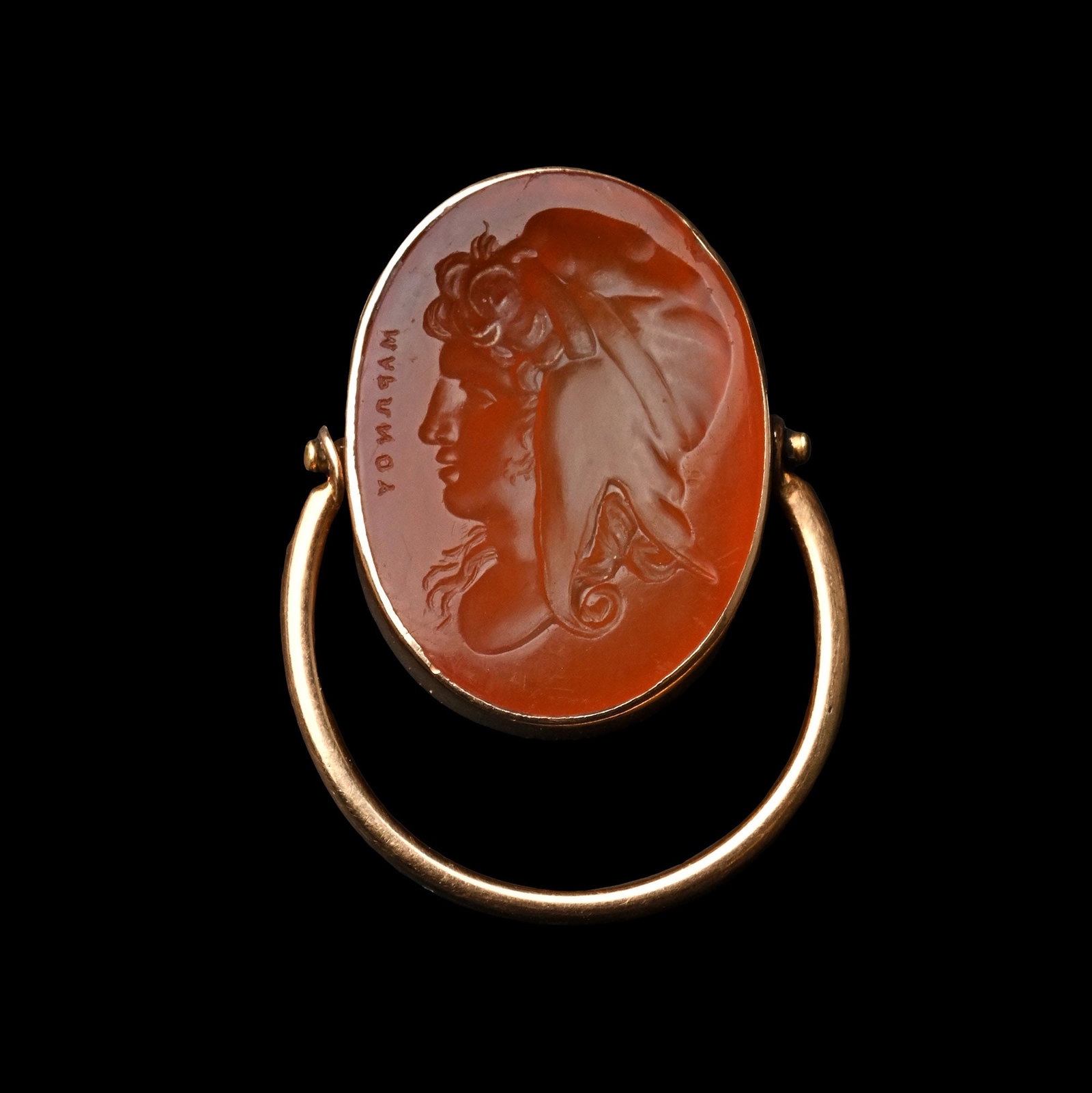 Carnelian Gemstone of the Prince of Troy in Gold Ring: Italy, 19th century A.D. An oval orange carnelian intaglio with a profile bust of Paris wearing a Phrygian cap, his long locks cascading from underneath it, a Greek pseudo-signature for Maronos on the