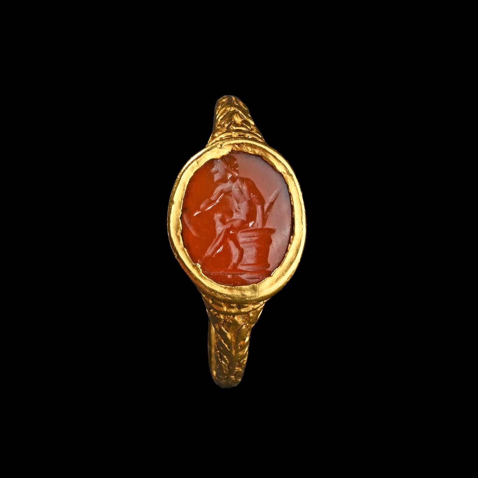 Renaissance Gold Ring with Carnelian Gemstone of a Resting Hero: Western Europe, 16th-early 17th century A.D. Comprising a round-section hoop with foliate decoration on the shoulders, oval setting with a beaded border and gadrooned underside, set with a dark carnel