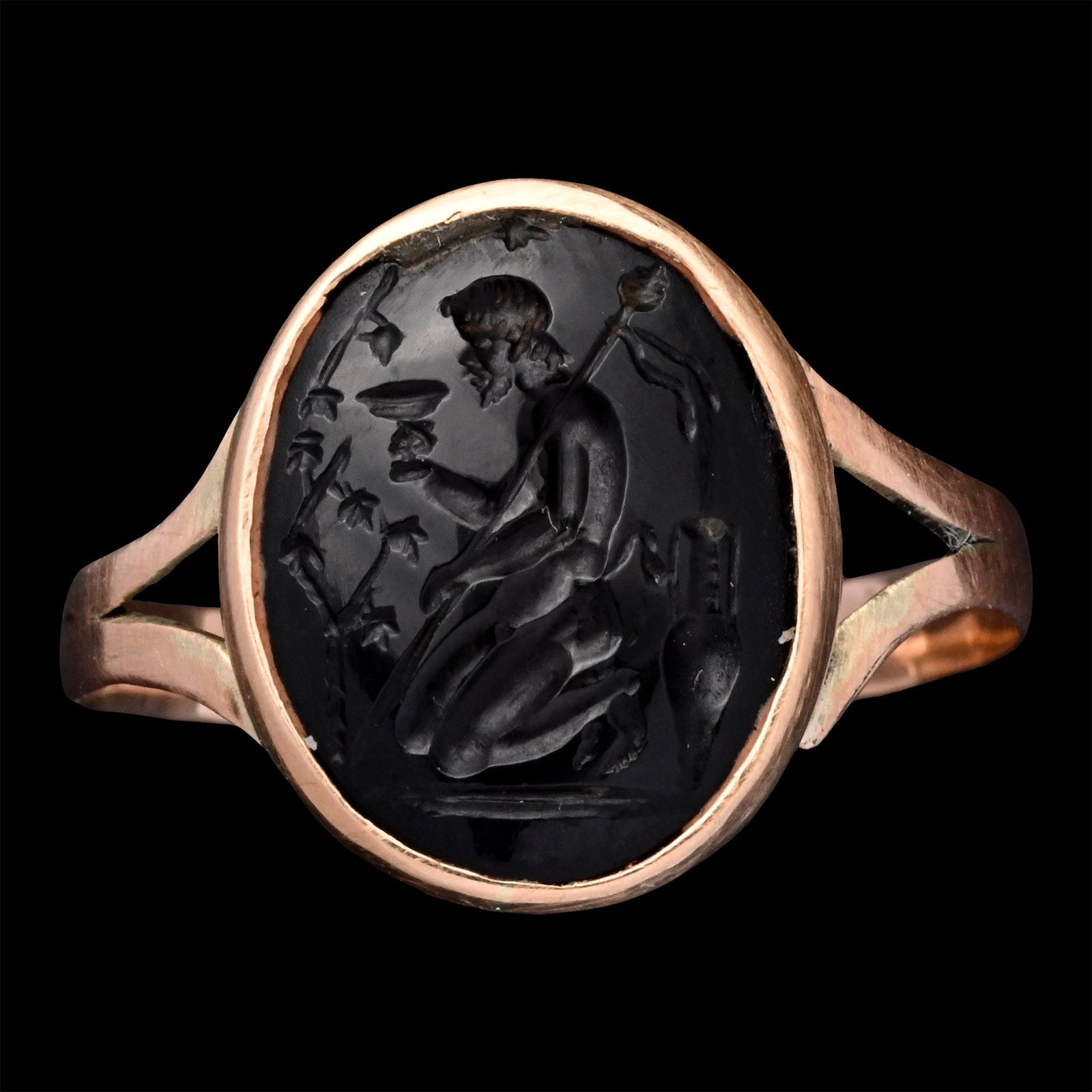 Renaissance Gemstone with Kneeling Satyr Drinking from a Goblet in Gold Ring: 19th century A.D. Black stone intaglio featuring a kneeling satyr before a grapevine, holding a large goblet in his right hand and a thyrsus in the crook of his left arm, a wine amphora behind him; se