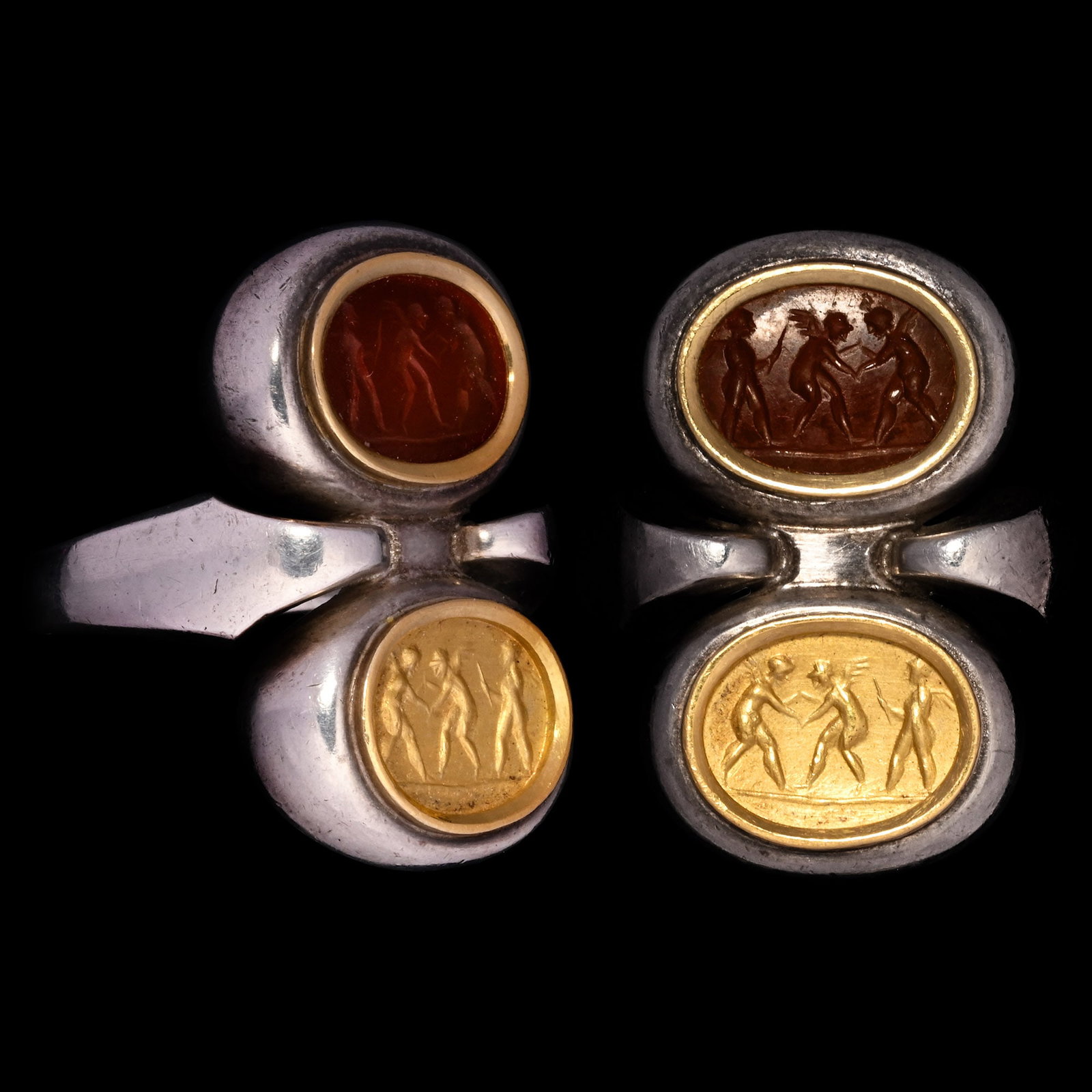 Roman Intaglio of Three Wrestling Erotes in Silver Ring: 1st-2nd century A.D. and later D-section hoop with widening lozenge-shaped shoulders supporting two discoid bezels; one with orange stone intaglio of three winged erotes, two engaged in a wrestling co