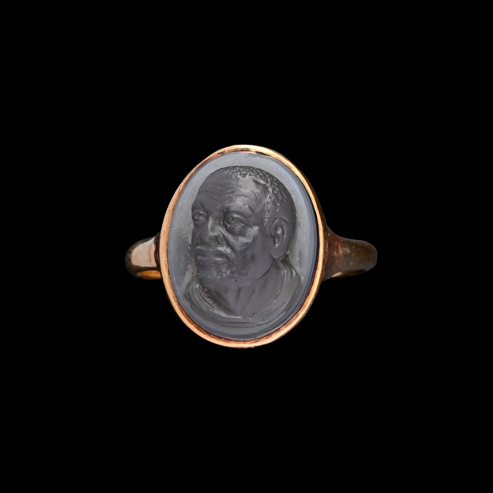 Antique Gold Ring with Agate Cameo of an African: Late 17th century A.D. D-section hoop and an oval bezel set with a grey banded agate cameo featuring a mature man in three-quarter view facing left, furrowed brow and short-cropped curly hair. 4.69 gr