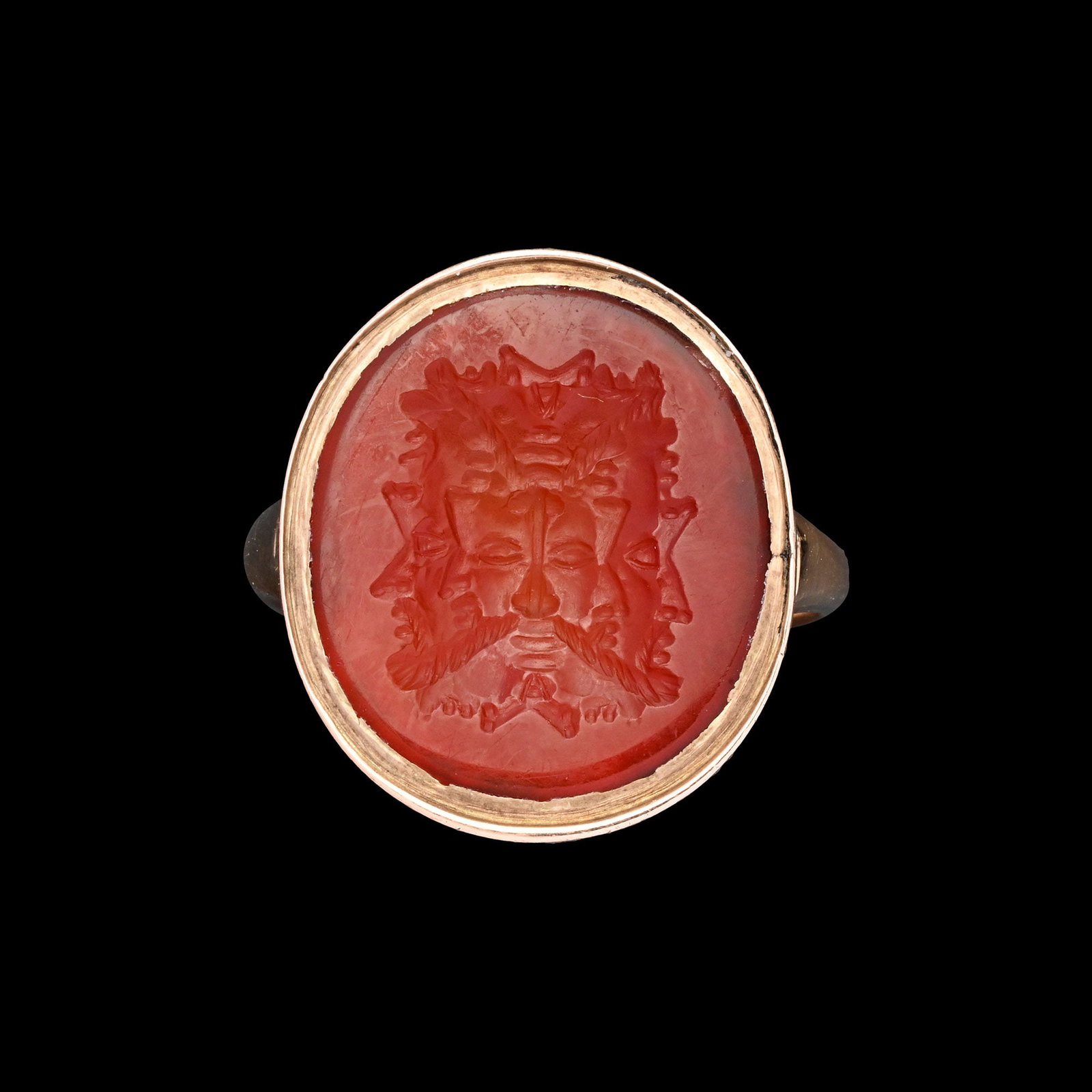 Post Medieval Gold Ring with Carnelian Gemstone with Fourteen Faces: Italy, 17th-18th century A.D. Composed of a D-section large hoop and an oval collet set with an intaglio intricately carved with a composite head composed of at least fourteen distinct faces, based on
