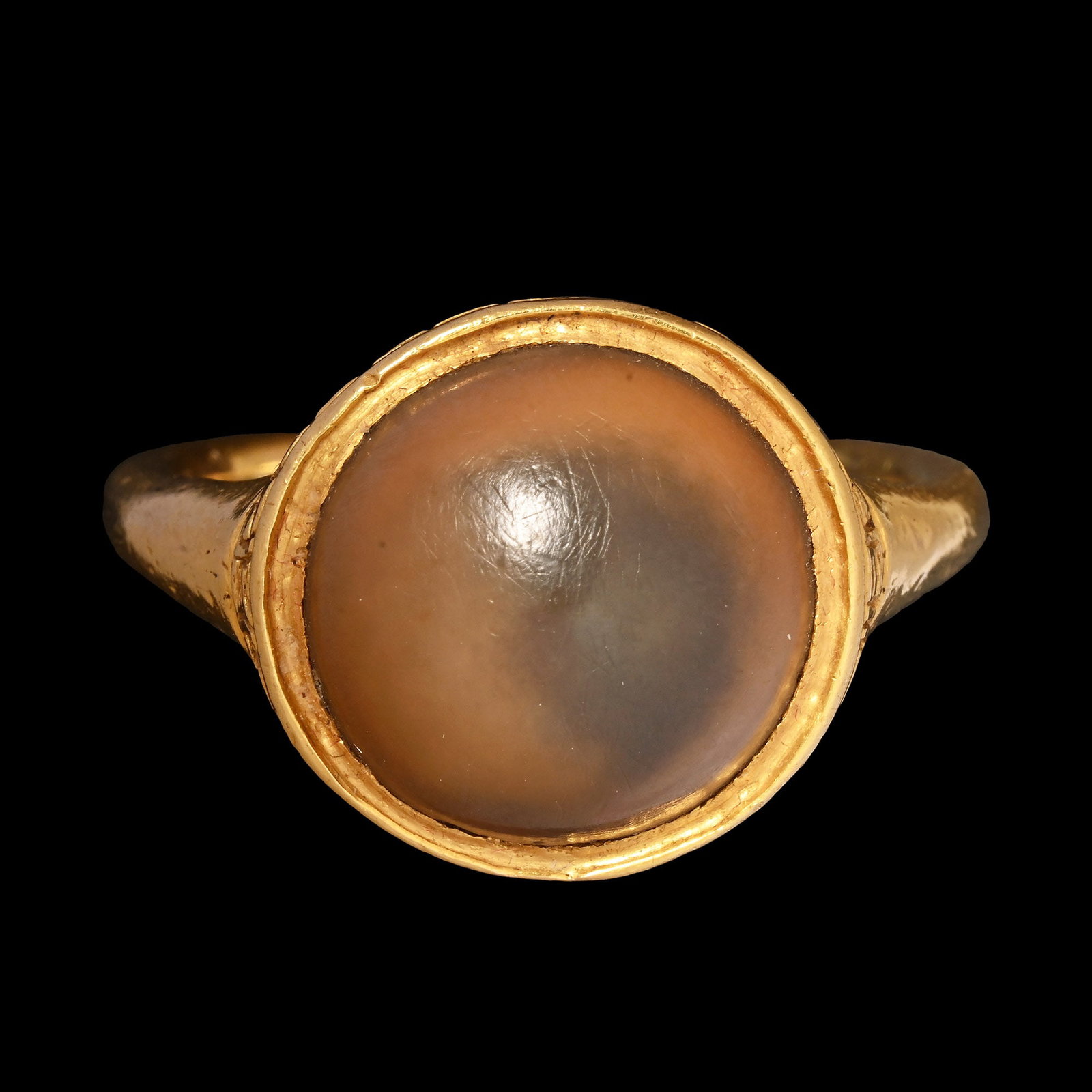 Renaissance Gold Ring with Toadstone: Western Europe, 16th century A.D. Featuring a round-section large hoop expanding towards the shoulders, a large circular bezel with a Greek key motif encircling the outer rim and set with a brown 'toa