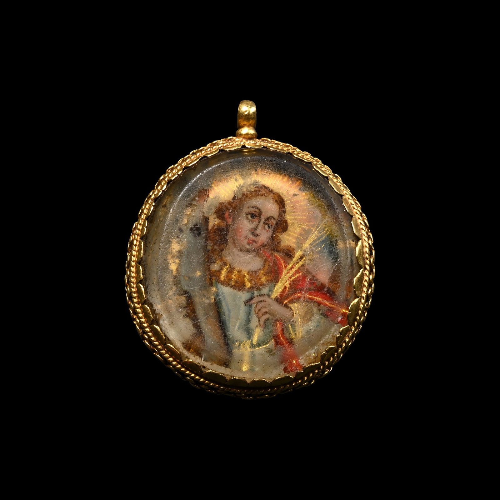 Bourbon Era Gold Devotional Pendant with Verre Eglomise Miniatures of Saint Catherine of Alexandria: Spain, circa 1700 A.D. Featuring a gold mount with twisted ropework border and scalloped edges securing bevelled glass coverings, one side depicting nimbate Saint Catherine of Alexandria wearing a pal