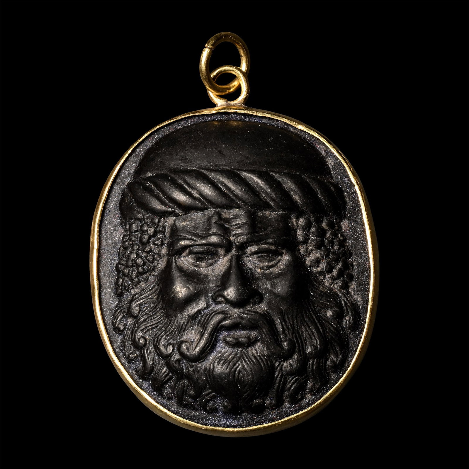 Gold Pendant with Glass Head: 19th century A.D. In low-relief, facing bust with braided band to his brow and bunch of grapes to each temple. 11.5 grams, 44 mm (1 3/4 in.). Private collection, Europe. Acquired on the English art ma