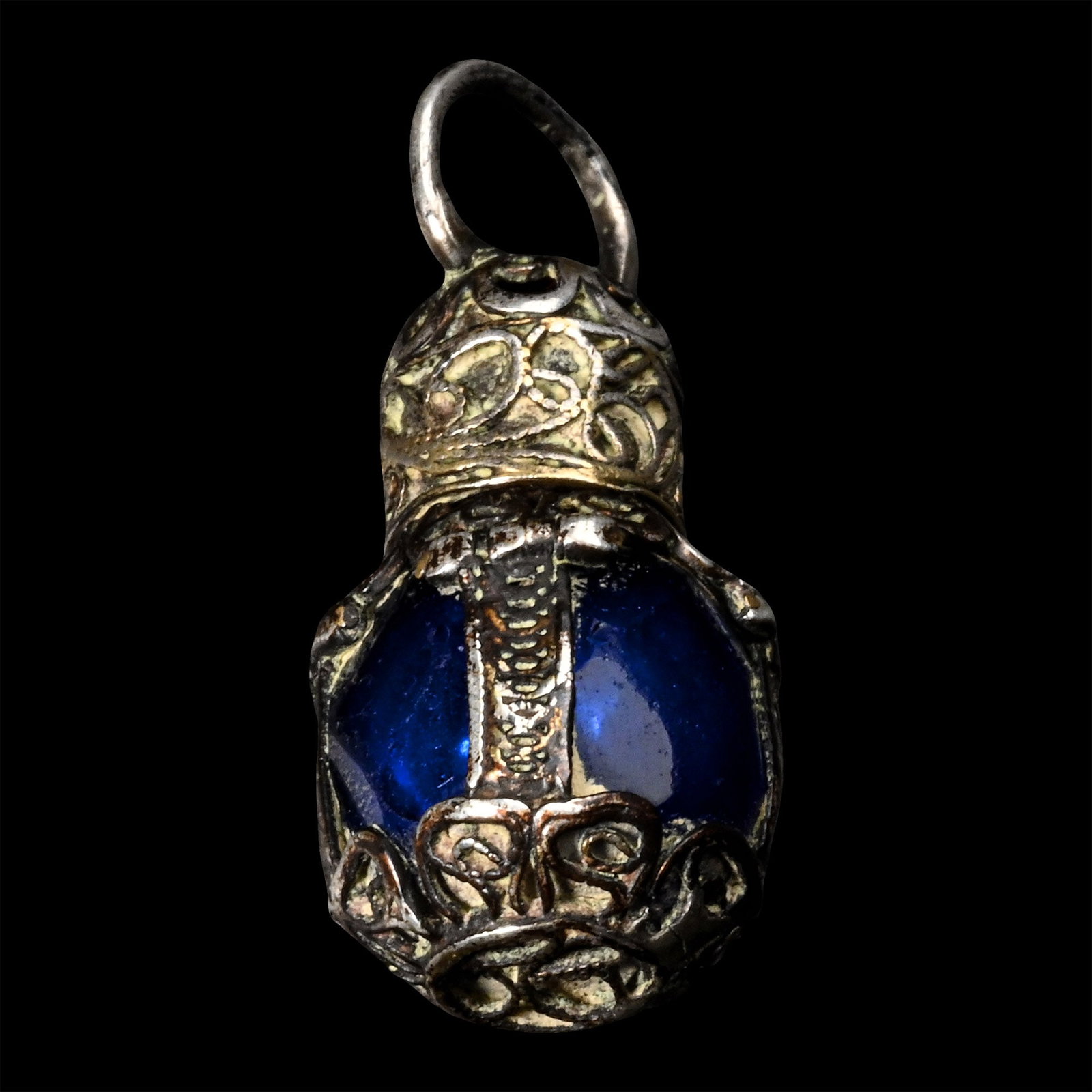 Miniature Blue Glass Scent Bottle with Silver Filigree Mounts: England, 17th century A.D. Of facetted deep blue glass, enclosed within an elegant silver filigree cage mount retaining traces of its original gilding; the domed screw-cap similarly decorated with scr