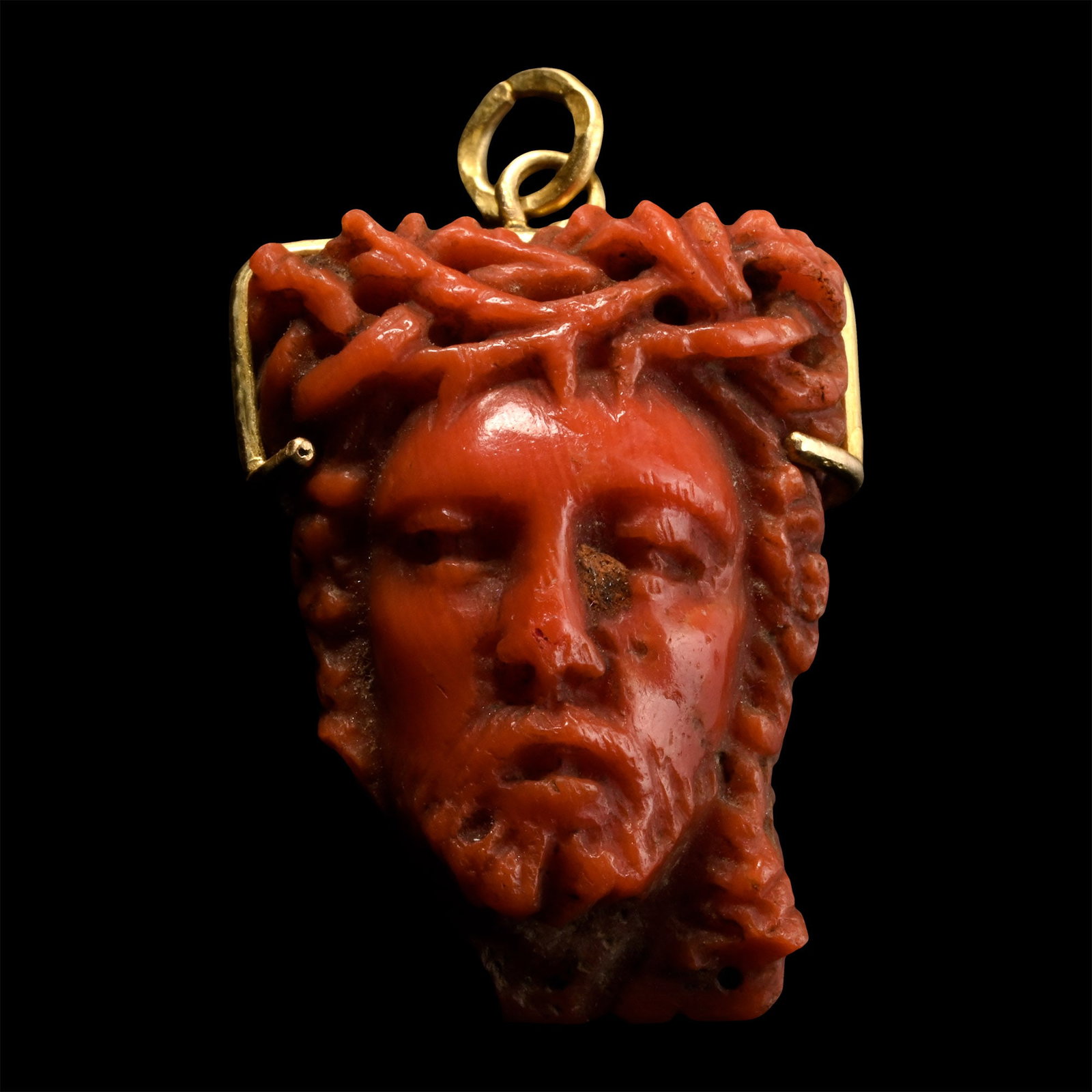 Post Medieval Coral Memento Mori Janus Chaplet Bead with Head of Christ and Skull: 17th-18th century A.D. Devotional prayer bead featuring a grimacing skull on one side and the other with the face of Jesus wearing the crown of thorns; set in a simple gold frame with suspension loop.