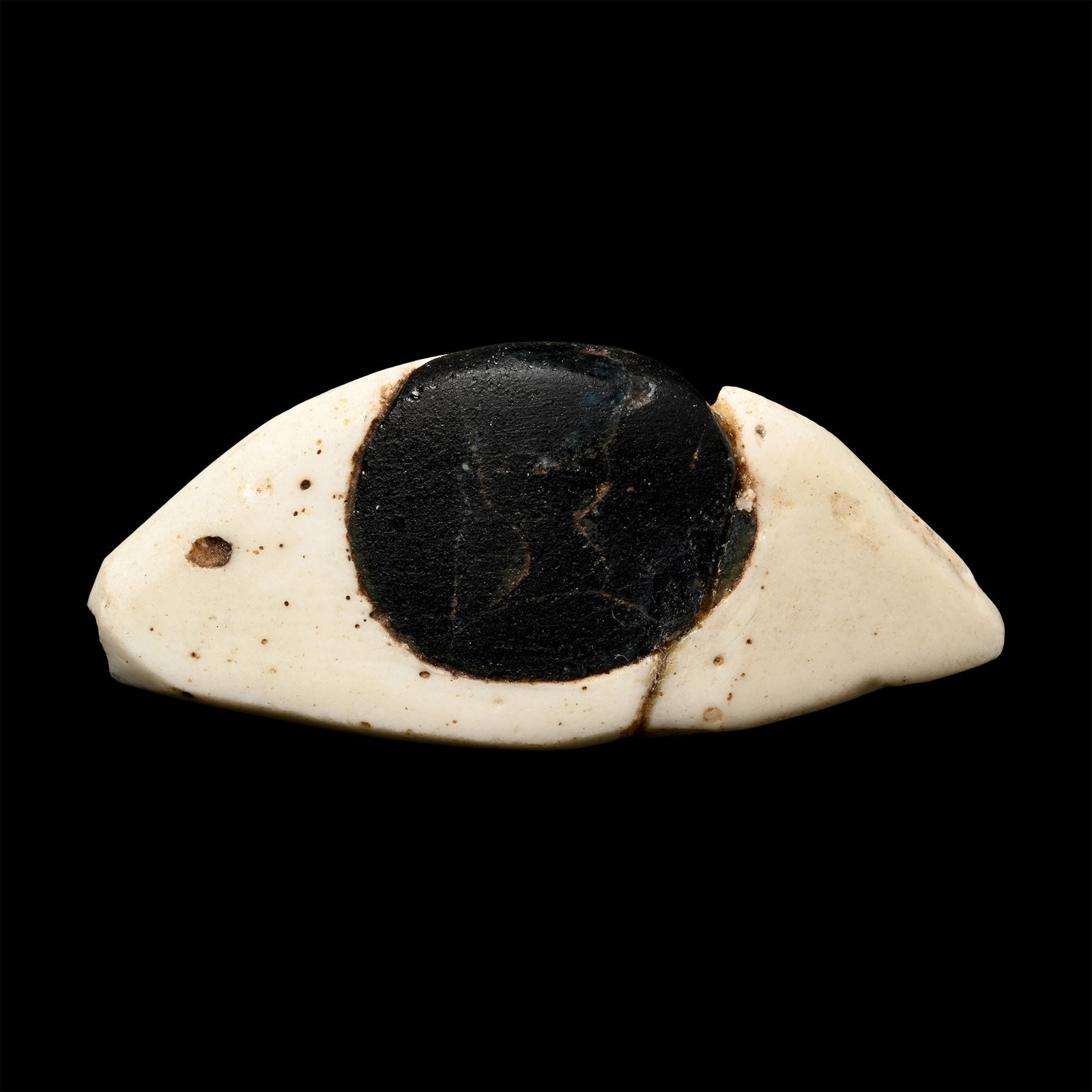 Egyptian Glass Mummy Eye: Ptolemaic Period, circa 332-30 B.C. White sclera with inset black glass iris; old dealer's ticket with legend; repaired. 5 grams, 36 mm (1 3/8 in.). [No Reserve] Ex John Cummings Ltd., Lincolnshire, U