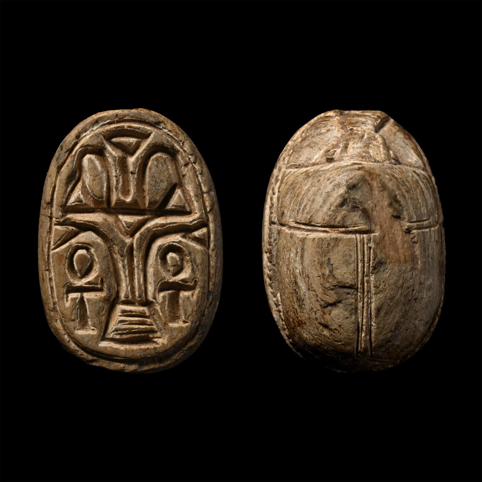Egyptian Steatite Scarab: Middle Kingdom-Second Intermediate Period, circa 1900-1560 B.C. Plano-convex in section with segmented carapace and mouth parts; to the underside, the 'Sema-Tawy' central motif and two flanking ankh g