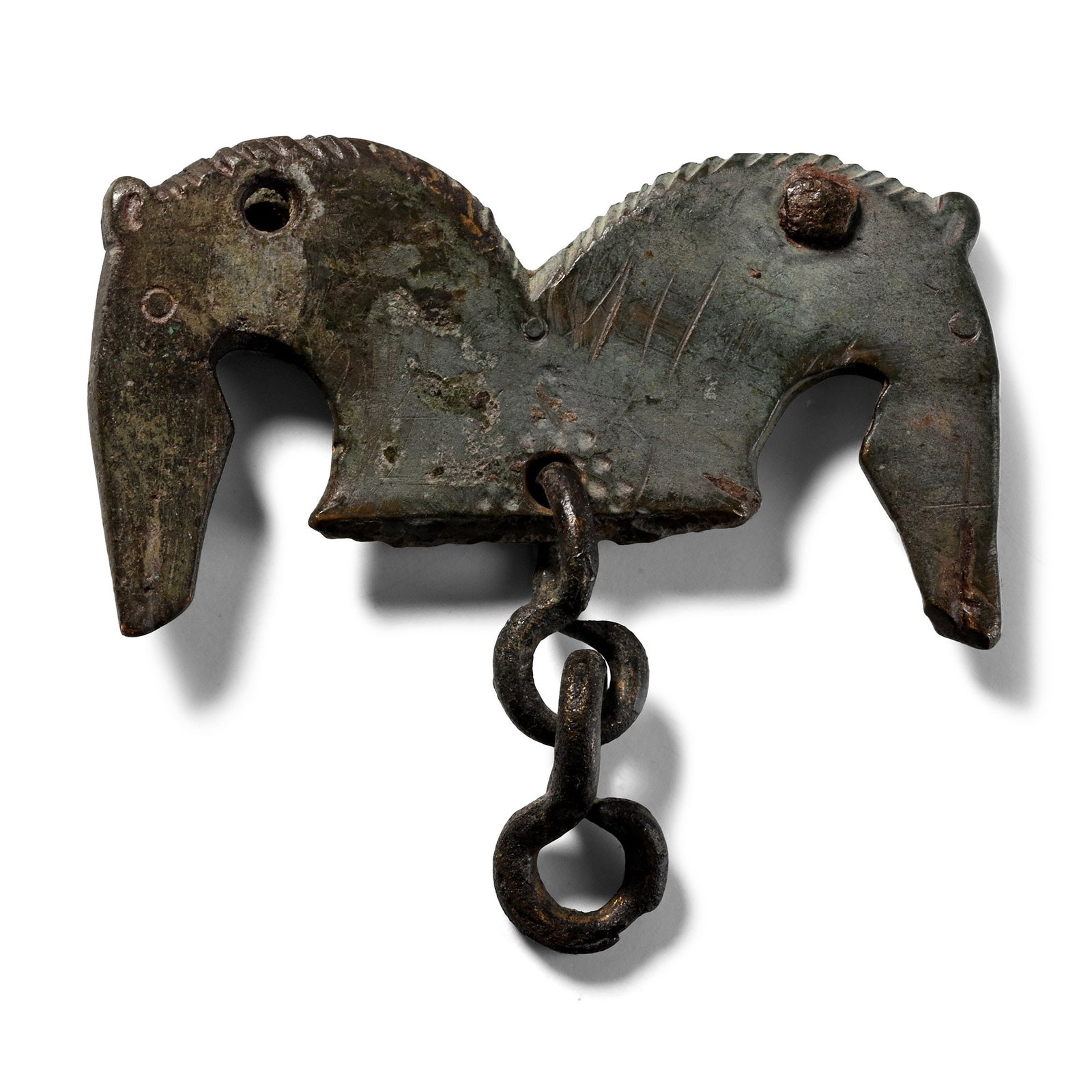 Roman Military Bronze Chape with Horse Heads: Circa 4th century A.D. Composed of two arching horse heads with annular eyes and notched manes, a small length of chain suspended from the lower edge. 16.5 grams, 47 mm (1 7/8 in.). Ex collection of a