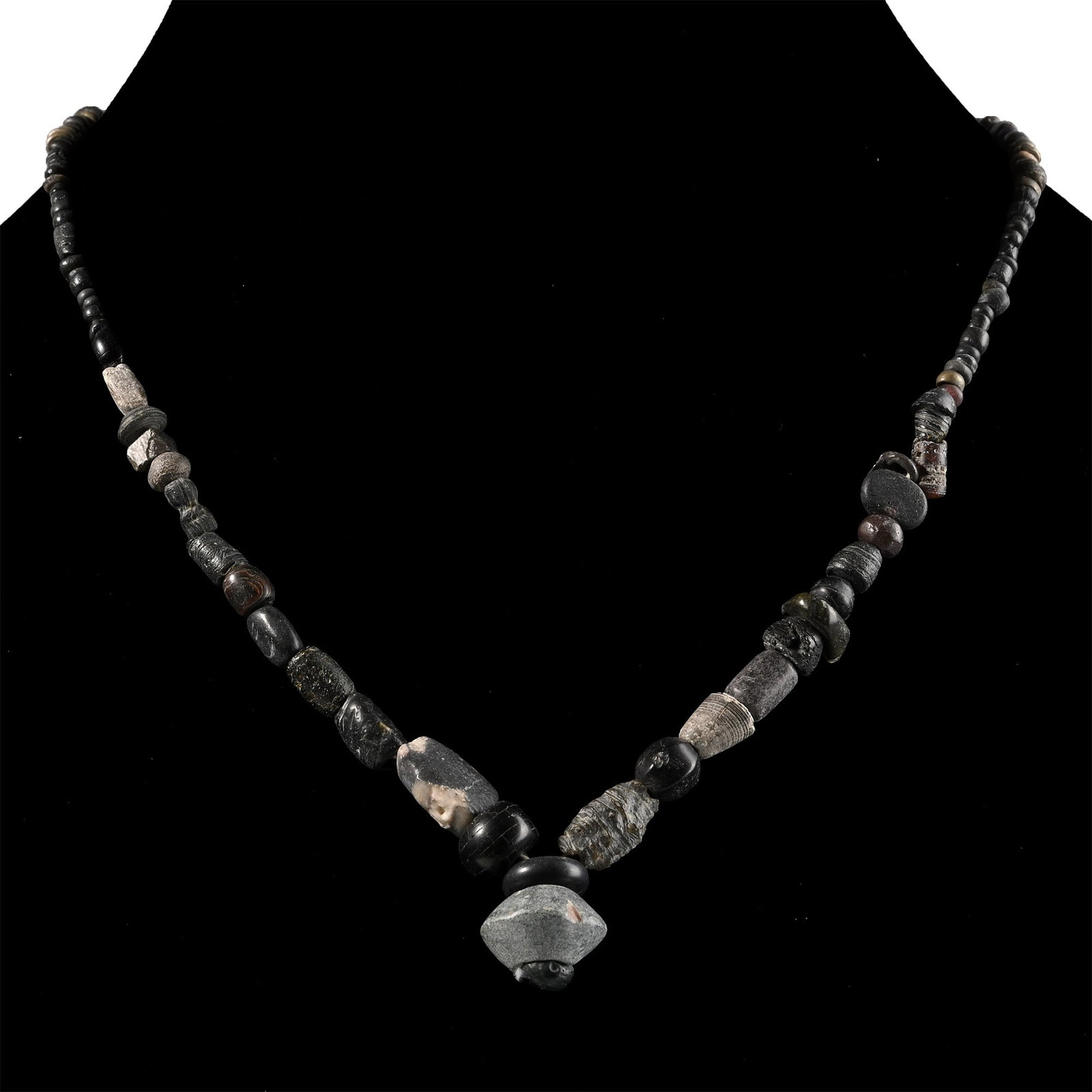 Roman Black Glass and Other Bead Necklace String: 1st-4th century A.D. and later. Graduated group of mixed beads, the central feature a large biconical bead; restrung. 16.7 grams, 34.6 cm (13 5/8 in.). [No Reserve] Acquired in the 1990s. Ex London,