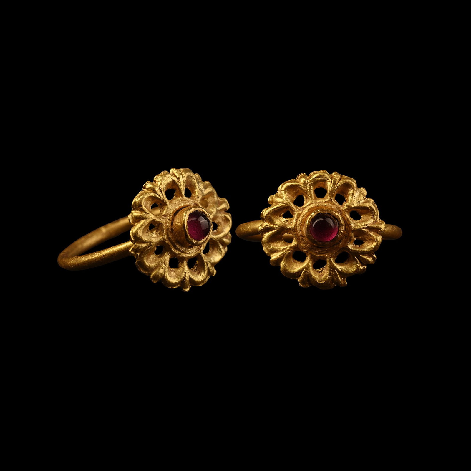 Roman Gold Ring with Garnet Cabochon: 3rd-4th century A.D. Comprising an openwork rosette bezel with interstitial pellets between the petals, central cell with inset garnet cabochon. 2.55 grams, 22.48 mm overall, 17.72 mm internal diamete