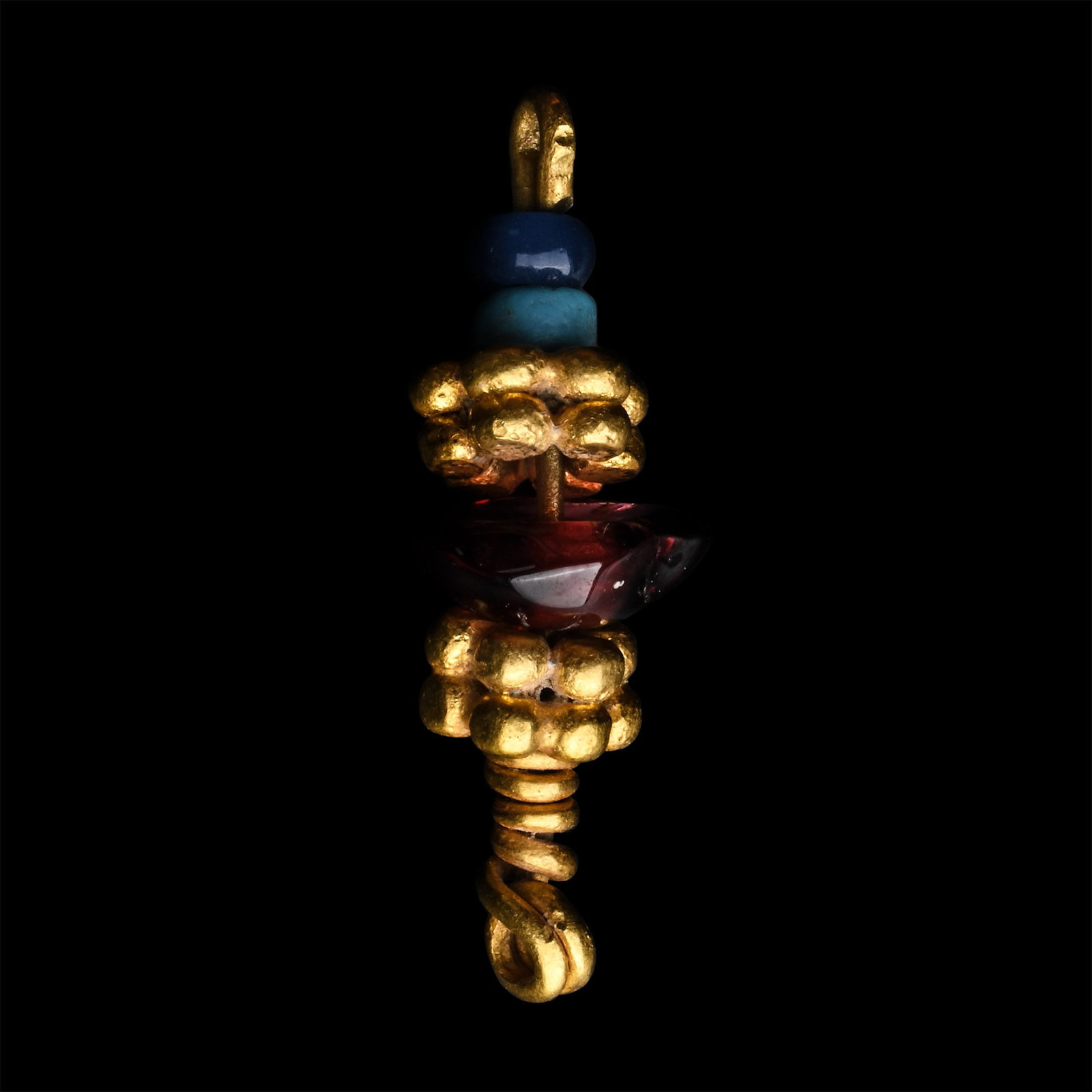 Western Asiatic Gold Pendant: Circa 1st millennium B.C. Formed with two granulated gold beads separated by a garnet bead, and two small blue beads below, a loop above and below. 2.41 grams, 22 mm (7/8 in.). Ex late Japanese gentle