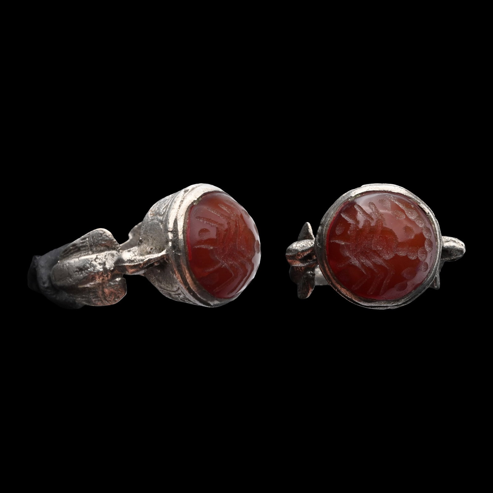 Bedouin Ring with Birds on Shoulders: Circa 18th-19th century A.D. White metal ring with the shoulders formed as birds with spread wings, conical bezel set with a carnelian cabochon engraved with a scorpion. 10.16 grams, 32.39 mm overall,