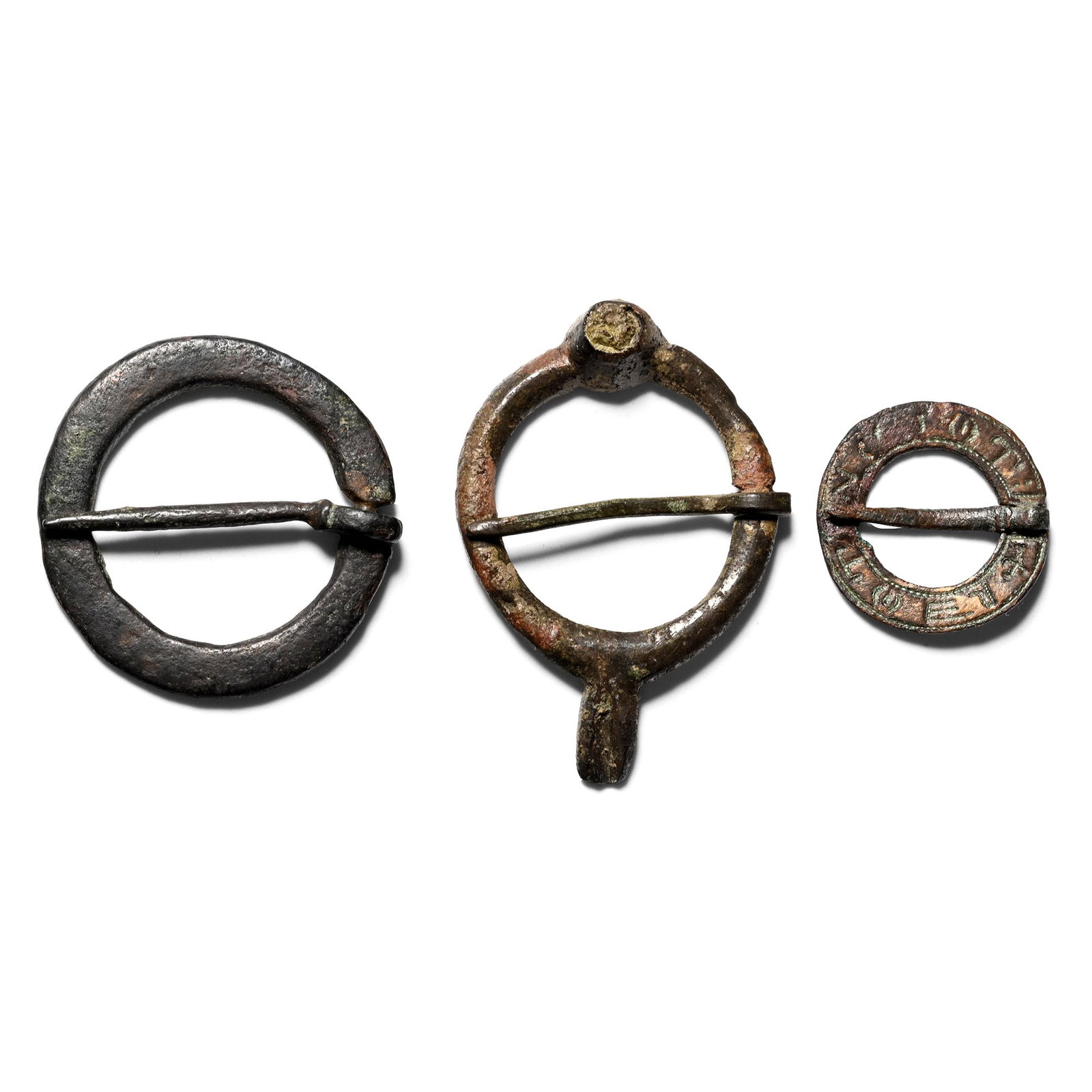 Medieval Bronze Ring Brooch Group: Circa 13th-15th century A.D. Comprising three annular brooches, one with floral motifs, one with a raised cell with traces of inlay, and the smallest with an inscription of meaningless letters. 5.86 g