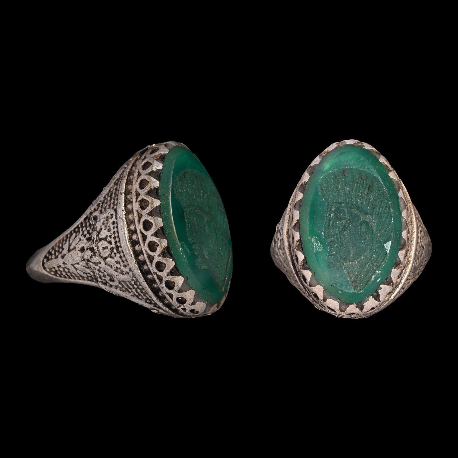 Bedouin Silver-Coloured Metal Ring with Gemstone: 20th century A.D. Keeled hoop with decorative panels on the shoulders, oval bezel set with a green glass cabochon with a profile bust. 12.24 grams, 32.81 mm overall, 19.86 mm internal diameter (approx