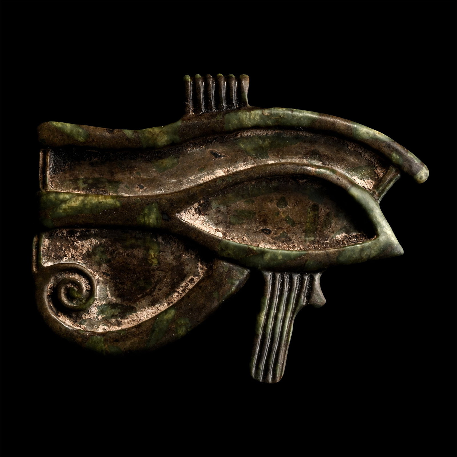 Egyptian Style Green Porphyritic Stone Eye of Horus Pendant: 20th century A.D. Carved from mottled stone wedjat with raised eyebrow, sclera, teardrop and markings, ribbed suspension loop above. 15 grams, 48 mm (1 7/8 in.). Old French collection. UK private coll