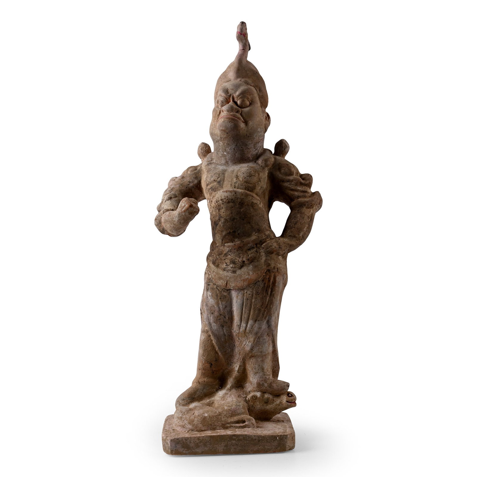 Chinese Tang Guardian Soldier Figure: Tang Dynasty, 618-907 A.D. or later. Modelled armoured and triumphantly trampling a creature beneath his feet, his helmet topped with a fierce-looking mythical bird, his right arm raised with clenched