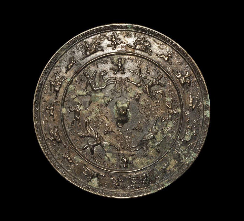 Chinese Style Massive Bronze Mirror with Animals: An undated archaistic cast bronze mirror with one polished face; the reverse with a central pierced lug in the form of a recumbent animal surrounded by huntsmen with spears and bows, and animals among