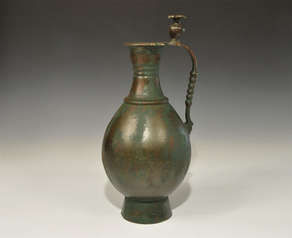 Islamic Style Bronze Jug: An undated archaistic cast jug, piriform in profile with flared base, waisted neck, everted rim, round-section handle; above the handle a knop with rosette finial. 1.5 kg, 35.5 cm (14"). Acquired on t
