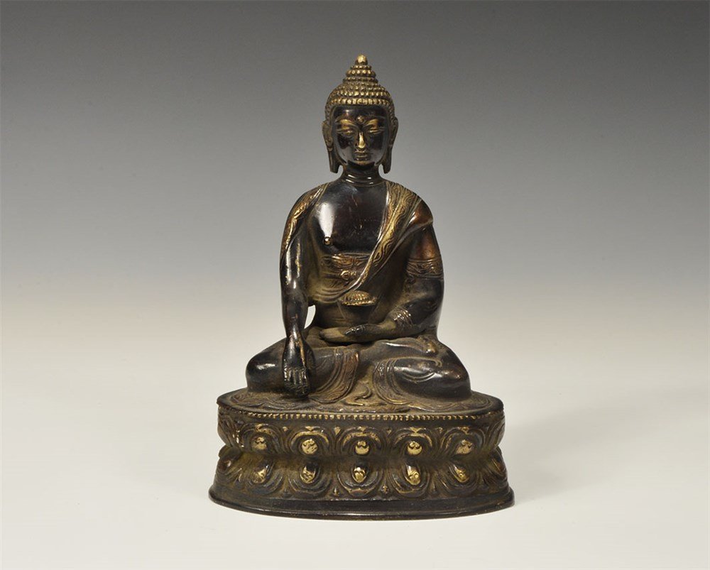Indian Style Parcel-Gilt Bronze Buddha Statuette: An undated archaistic cast figurine of the Buddha seated cross-legged on a lotus throne, holding a lotus blossom in the left hand; hollow to the underside. 1.4 kg, 19 cm (7 1/2"). Property of a London