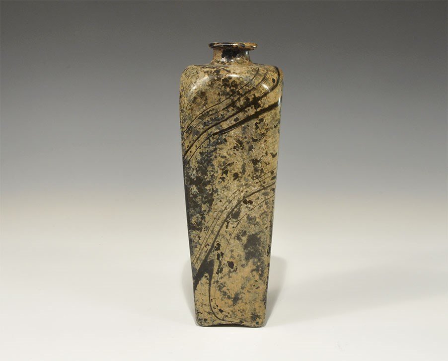Islamic Style Glass Bottle: 19th century AD. A tall black glass bottle with ochre swirls, square in plan with rounded shoulders and everted rim. 565 grams, 22.5 cm (8 3/4"). Acquired on the London art market before 1995.