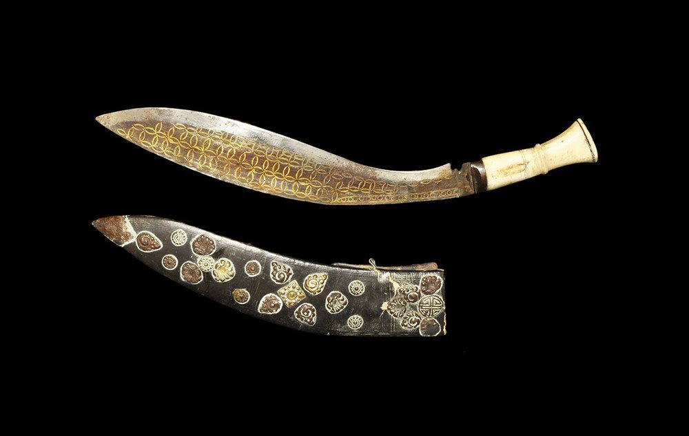 Nepalese Steel Brass-Inlaid Kukri and Scabbard: 19th century AD. A kukri in its leather scabbard with wooden frame; the single-edged blade curved with punched roundels to one face, intersecting inlaid circles to the other; waisted bone grip with en