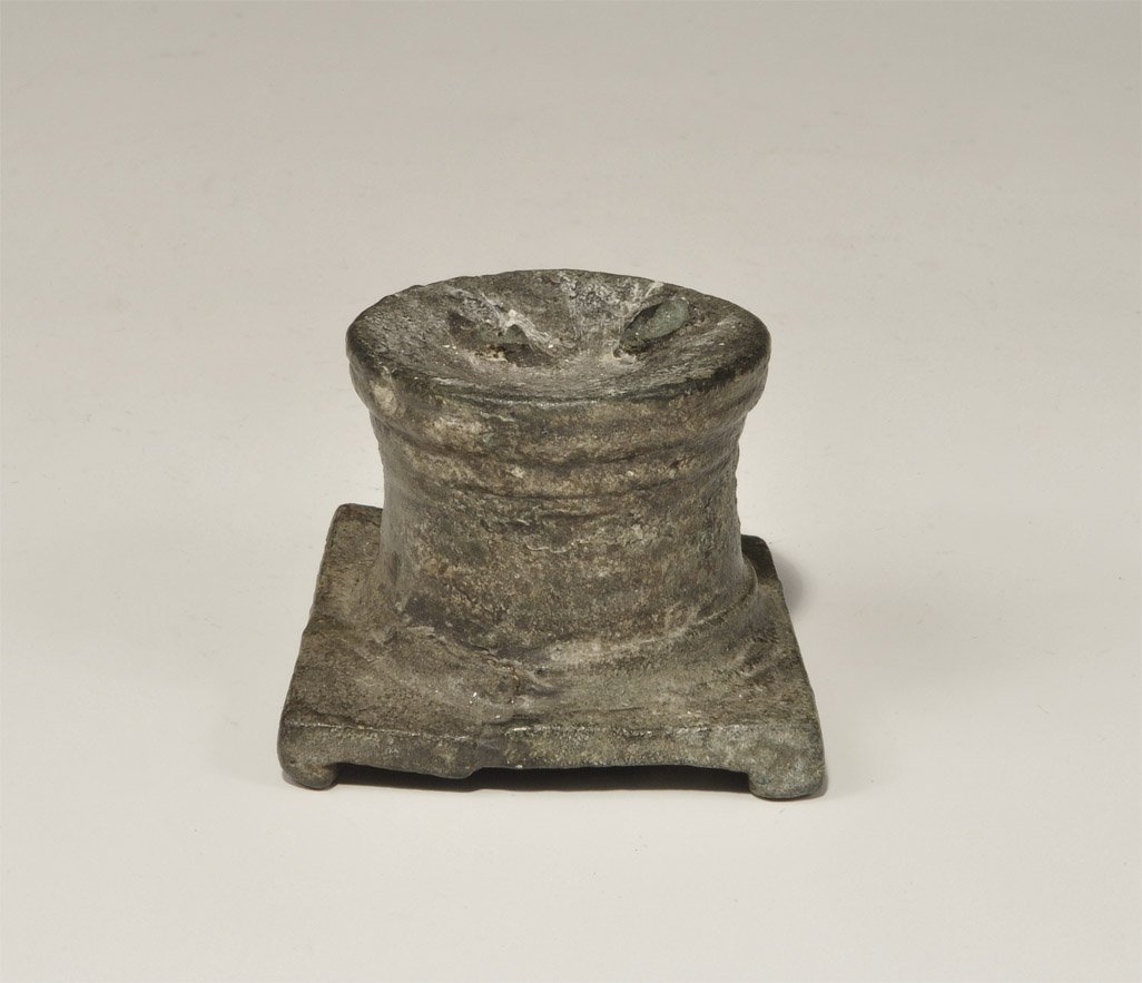 Roman Bronze Statuette Base: 1st-3rd century AD. A cast bronze figurine base with square lower edge, four stub feet and columnar body; remains of the figurine's two feet on the upper face. 186 grams, 42 mm (1 3/4"). Property of a