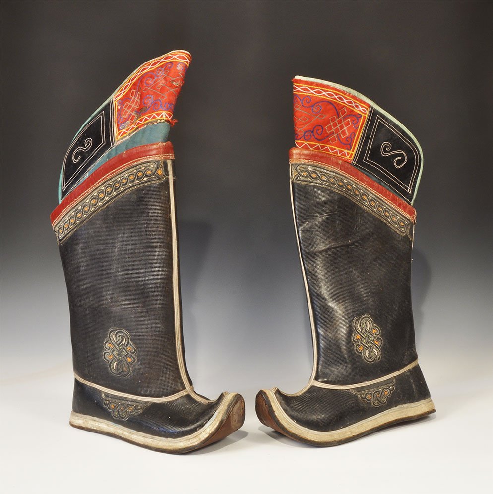Chinese Tibetan Leather Ornamented Boot Pair: 20th century AD. A pair of hand-made leather boots, each with textured brown leather surface, stitched leather soles, moulded leather ornamental panels, guilloche band to the upper, separate fabric in