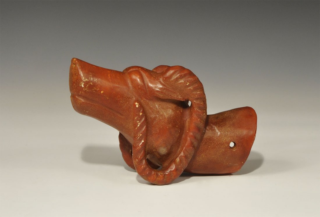 Chinese Tibetan Stone Ram's Head Finial: An undated archaistic red stone finial in the form of a ram's head with lentoid eyes and c-shaped horns; the neck hollow to the reverse, pierced in two places for attachment. 1.7 kg, 20 cm (8"). Prope