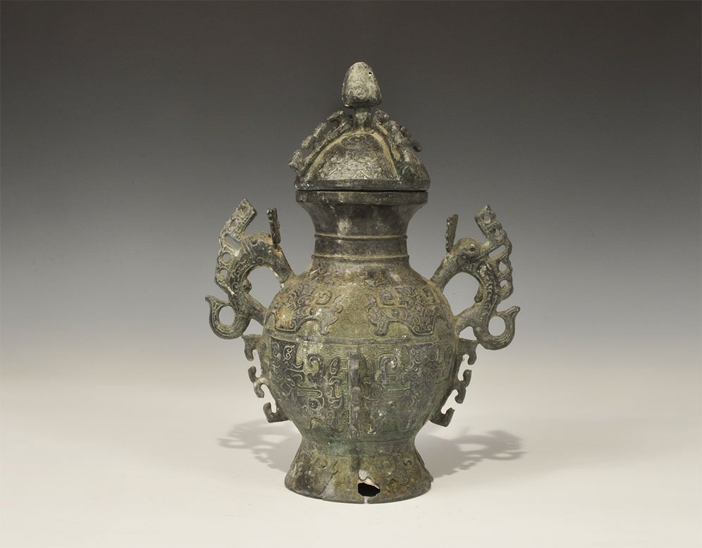 Chinese Style Bronze Lidded Vessel with Dragon Handles: Am undated archaistic cast vase with flared base and ovoid body and geometric detailing, two dragon handles to the shoulders and waisted neck; separate domed lid with knop handle. 1.5 kg, 27.5 cm (10 