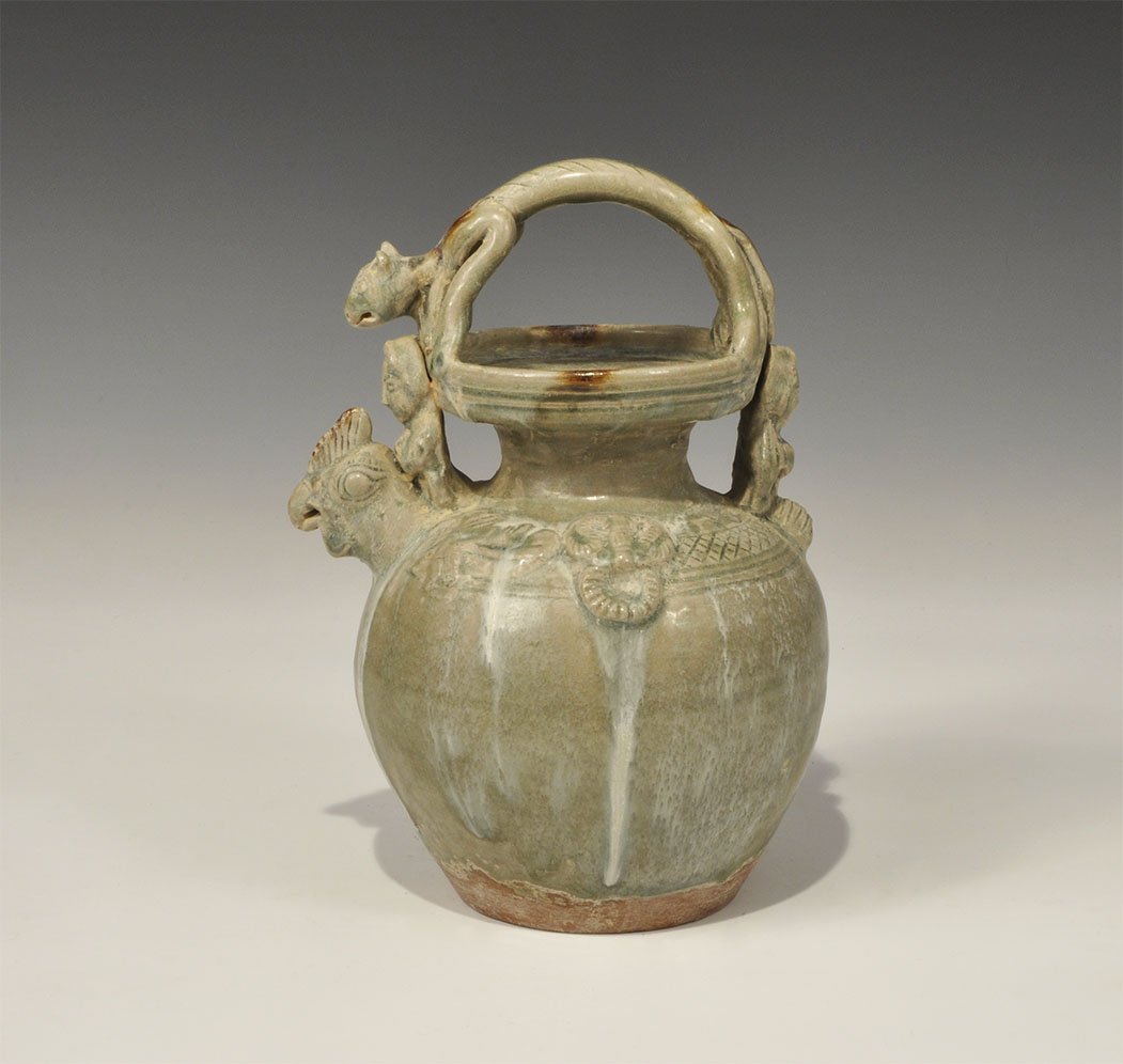 Cambodian Style Ceramic Jug with Figures and Animals: An undated archaistic green-glazed ceramic jug with broad neck and band of ornament to the shoulder; the rim of the neck with seated female supporters, bird-head spout; the round-section handle a cat.