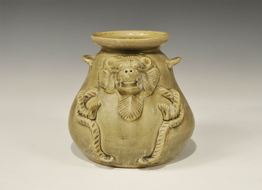 Cambodian Style Ceramic Vessel with Animal Mask: An undated archaistic green-glazed pot with bulbous body, flange rim; applied animal-head detailing, loops to the shoulder. 1.3 kg, 16 cm (6 1/4"). Property of a London collector, acquired before 1990