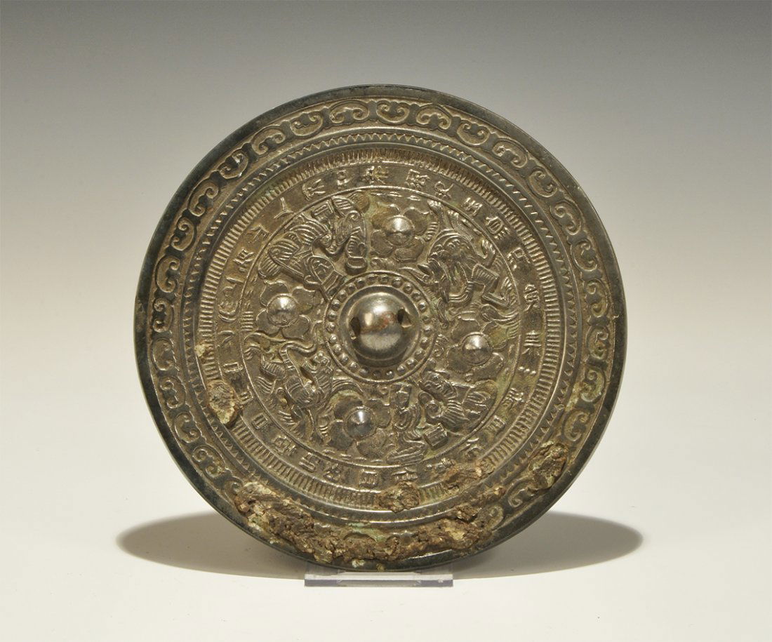 Chinese Style Bronze Epigraphic Mirror with Humans and: An undated archaistic discoid mirror with one polished face; to the reverse a central pierced lug surrounded by a band of humans and dragons, outer band of text. 727 grams, 18.5 cm (7 1/4"). Property