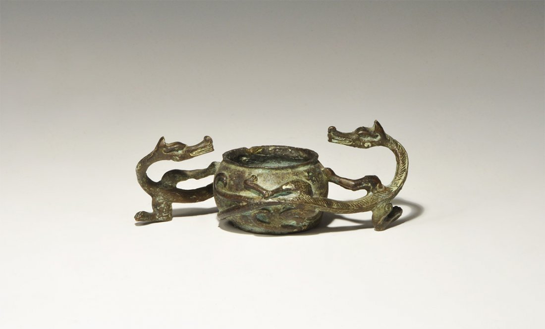 Chinese Style Bronze Dragon-Handled Vessel: An undated archaistic miniature bronze caudron with roundd body and everted rim, the handles formed as integral serpentine regardant dragons coiled around the pot. 288 grams, 14 cm (5 1/2"). Property 