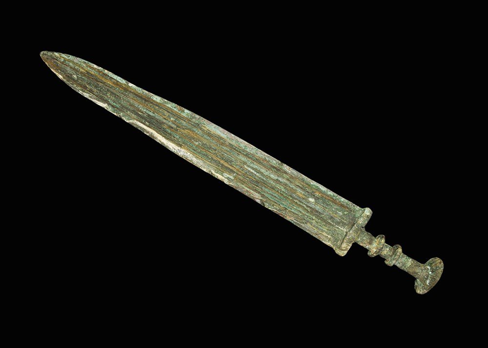 Chinese Bronze Short Sword: Han Dynasty, 206 BC-220 AD. A cast bronze short sword with central midrib to the gently waisted blade; elliptical guard, two transverse discoid collars to the grip and large discoid pommel above. 923 