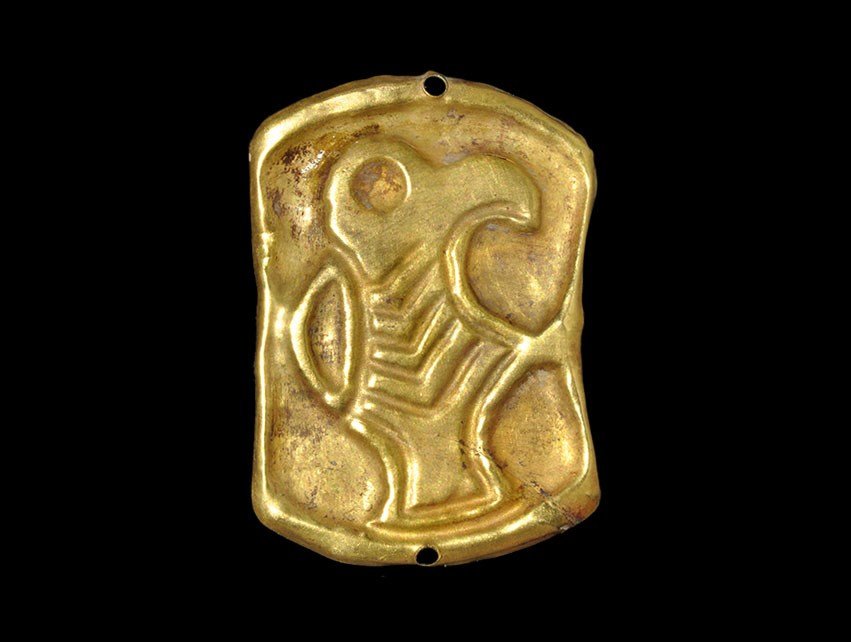 Merovingian Frankish Gold Bird of Prey Mount: 6th century AD. A repoussé gold foil mount of waisted elliptical form, the central field occupied by a bird of prey with hooked beak, D-shaped wing, chevron body and rectangular tail; two holes to ac