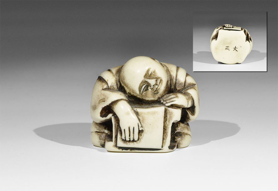 Japanese Composite Sleeping Scholar Netsuke: 20th century AD. A netsuke depicting a rotund scholar in a loose robe sleeping with his head resting on a scroll on his reading stand; two holes to the rear to accept the cord; two incised character s