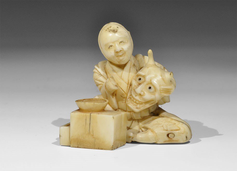 Japanese Antique Ivory Seated Figure with Hannya and: Late 19th century AD. A carved figurine of a boy sitting cross-legged with a bowl on a chest; in his left hand a large mask with gaping jaws and horns; the chest with two drawers, the lower one partly