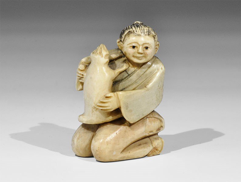 Japanese Composite Kneeling Figure: 20th century AD. A figurine of a girl kneeling, playing with a pet; the girl with long hair wearing a loose gown and sandals; green pigment to the robe, black to the hair and eyes, rose to the face, h