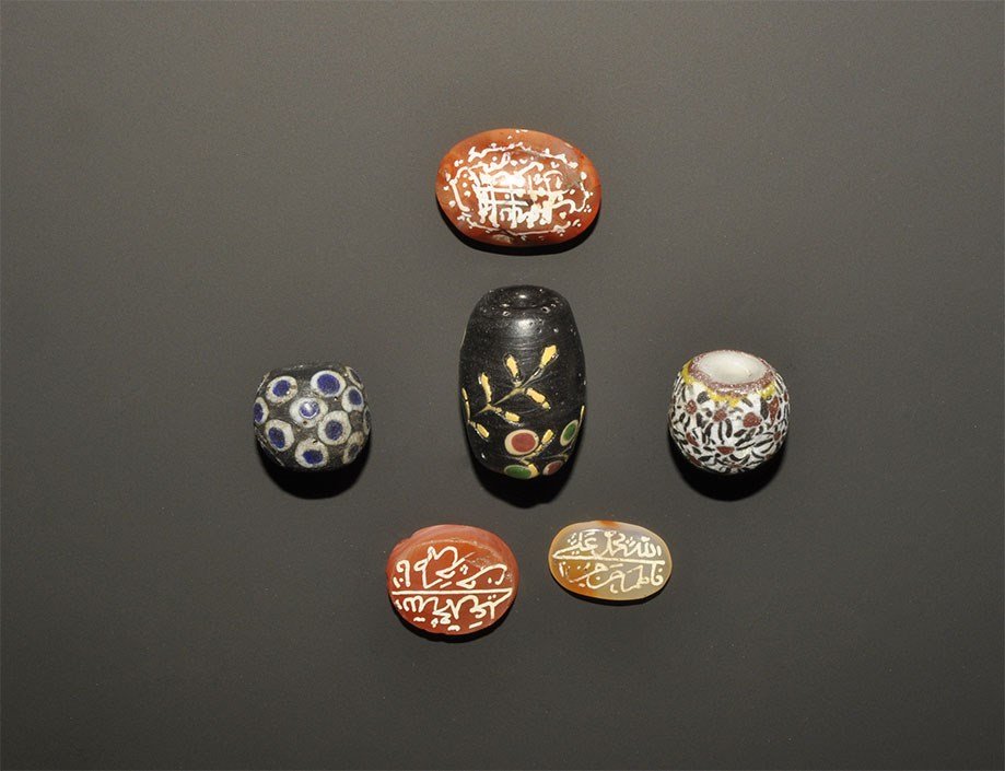 Islamic Style Calligraphic Seal and Bead Group: A mixed group of undated archaistic items comprising: three dark glass core beads with polychrome detailing; three carnelian plaques, each with calligraphic text. 47 grams total, 17-29 mm (3/4 - 1 1/4