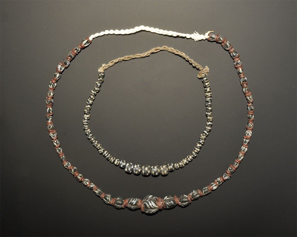 Islamic Style Glass Bead Necklace Group: A group of two restrung necklaces of undated archaistic beads comprising: one of graduated globular dark blue beads with white mosaic detail; one of graduated four-strand dark blue beads with red appl