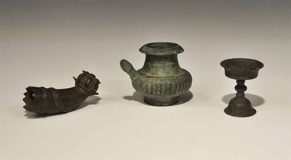 Far Eastern Bronze Artefact Group with Karhai Vessel: 16th century AD and later. A mixed group of bronze artefacts comprising: a miniature spouted vessel with flared base; a miniature chalice with bell-shaped base; a curved terminal with poppy-head finia