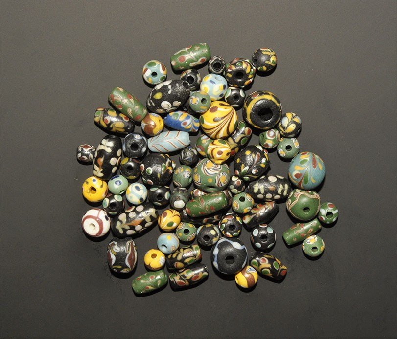Islamic Qajar Mosaic Bead Group: Qajar Dynasty, 1785-1925 AD. A mixed group of glass polychrome beads in fusiform and spherical profiles, mainly dark blue with yellow, red and white mosaic elements. 75 grams total, 6-16 mm (1/4 - 1/2