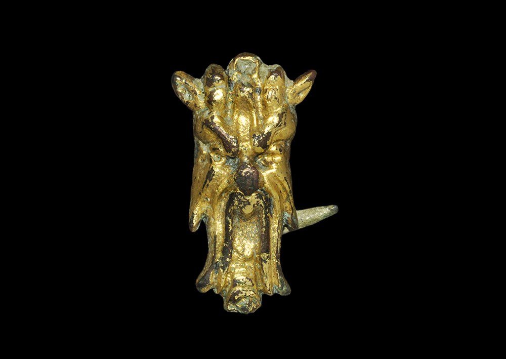 Post Medieval Gilt-Bronze Grotesque Mask Mount: 17th century AD. A cast mount, hollow to the reverse, in the form of a long grotesque mask with scowling brow, long pointed ears. 5.89 grams, 27 mm (1"). Acquired from an English collection in the ear