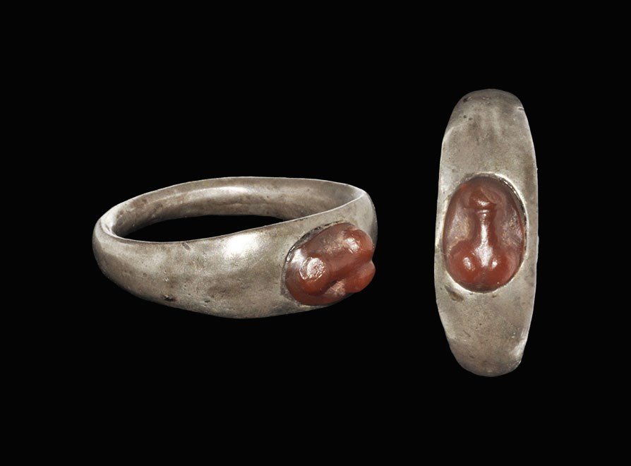 Roman Silver and Carnelian Cameo Ring with Phallus: 1st-2nd century AD. A finger ring comprising a D-section hoop and inset carnelian to the bezel with reserved phallus design. 5.69 grams, 25 mm overall, 18.18 mm internal diameter (approximate size Bri