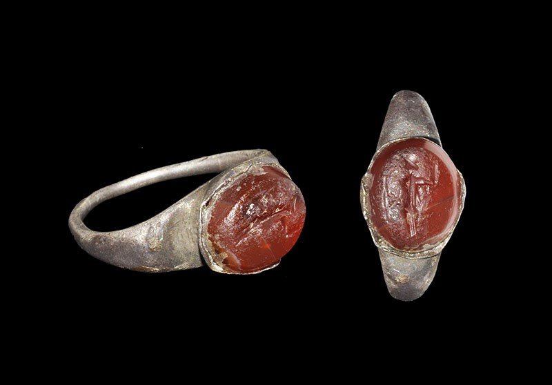 Roman Silver Ring with Carnelian Intaglio with Mercury: 2nd-3rd century AD. A round-section hoop with expanding shoulders, elliptical bezel with inset carnelian cabochon intaglio depicting Mercury with petasos, one hand raised. 2.02 grams, 24 mm overall, 1